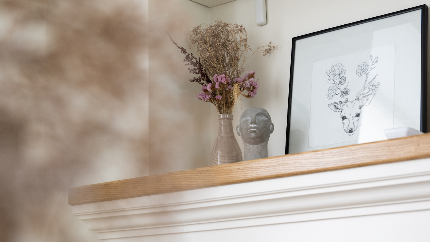 Shelf decor with framed art, dried flowers, and a sculpted head on a wooden mantel